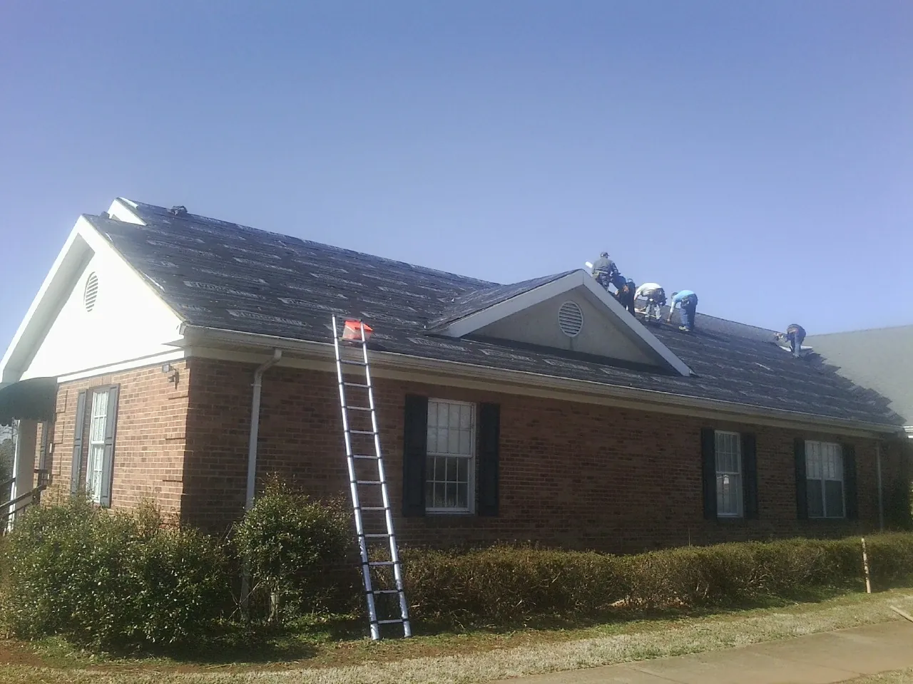 Crew tearing shingles off a brick ranch roof with a ladder set — Metal Roof Repair work by our crew in Gore