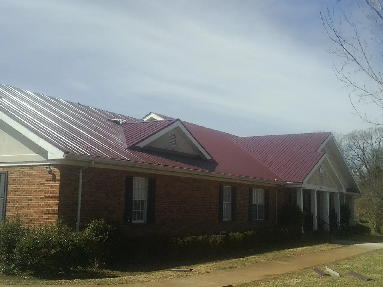 Red metal roof with gabled entries on a long brick building, from a Hail Damage Roof Repair job in Gore