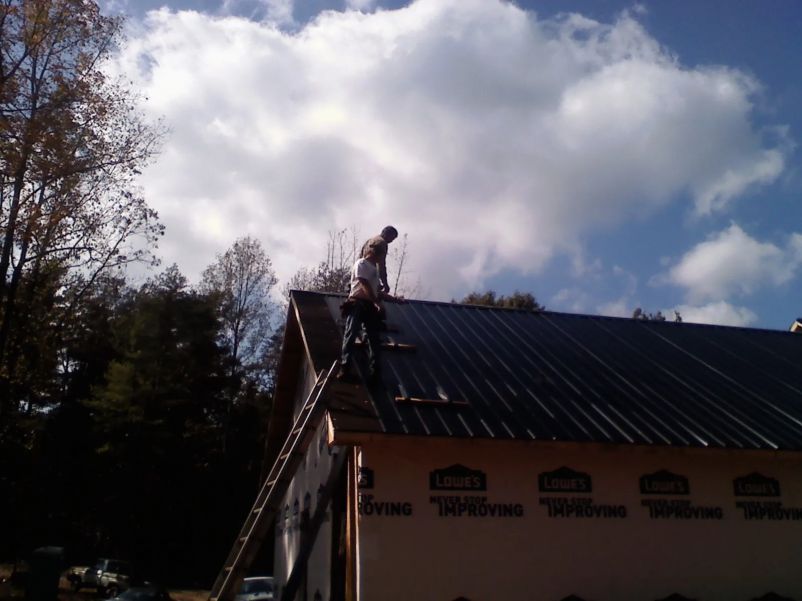 Roofer fastening dark metal panels high against a cloudy sky, from a Roof Inspection job in Gore