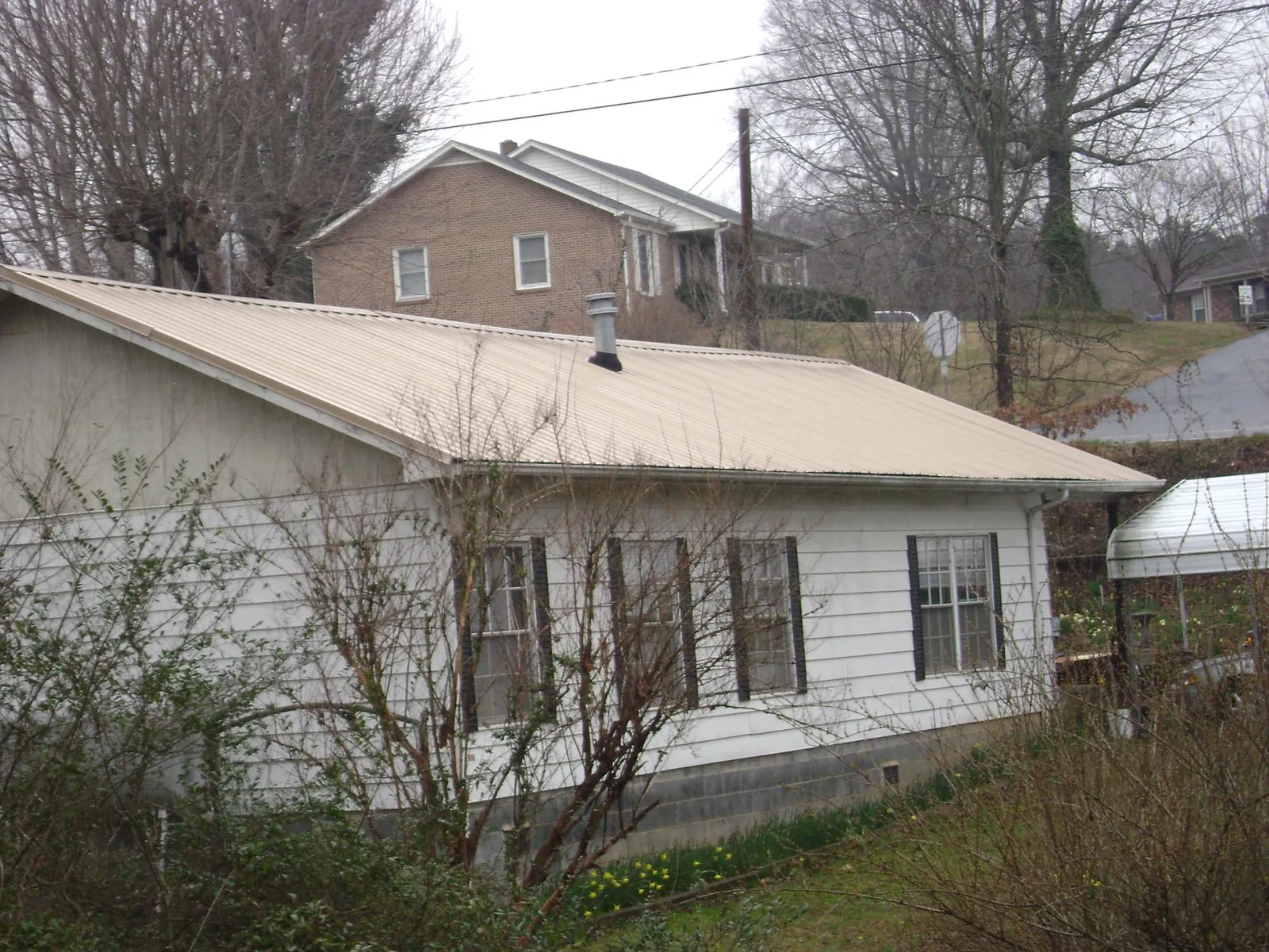 Tan metal roof on a white sided house set into a hillside — Commercial Roofing by Roofing Brothers in Gore