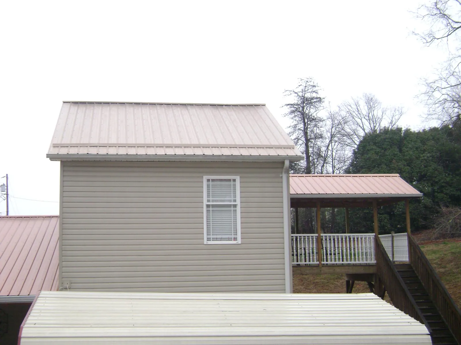 Tan metal roofs on a two story addition and attached porch, from a Roof Replacement job in Gore